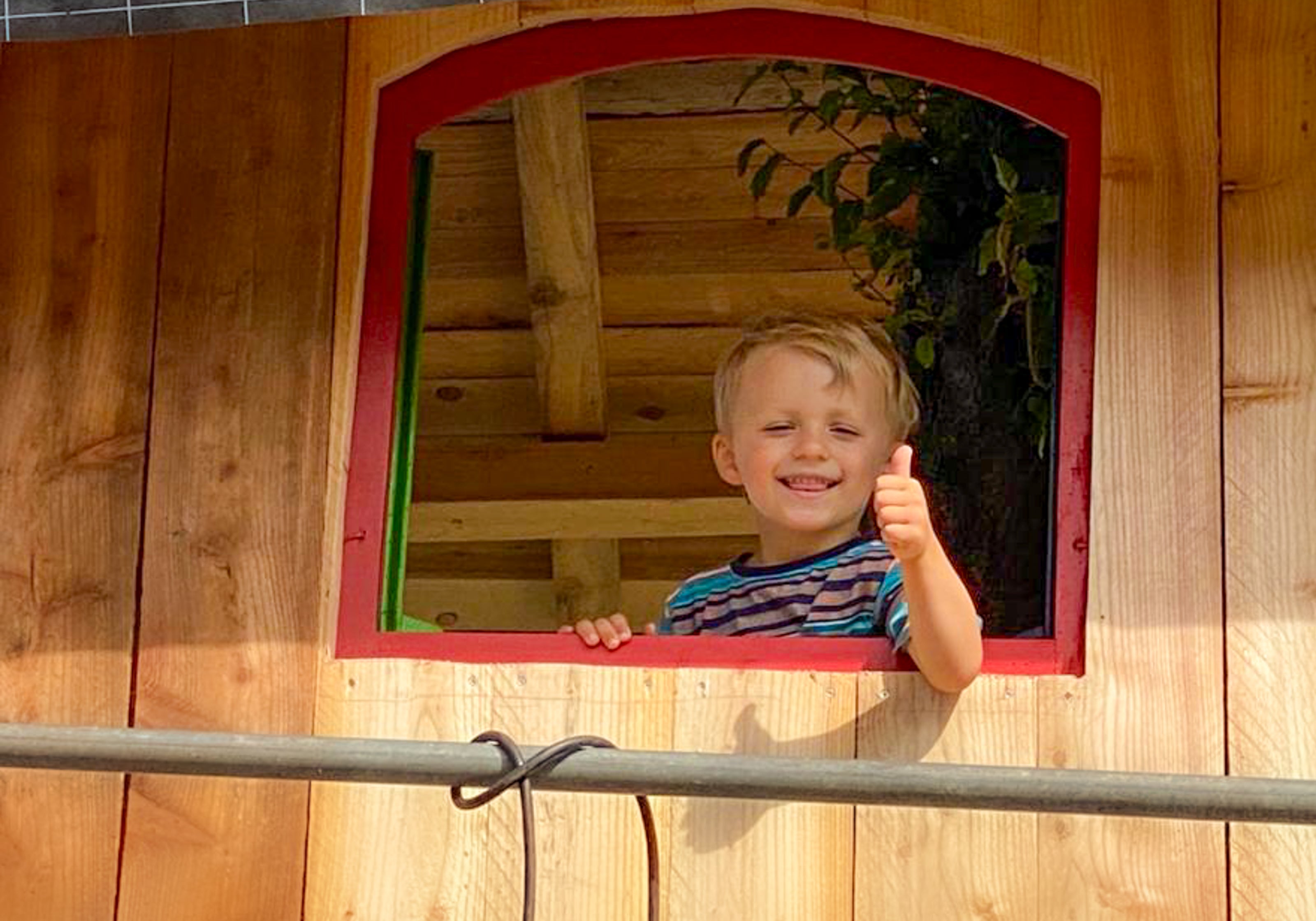 Baumhaus bauen mit Kind Kindertraum glückliches Kind schaut aus dem Fenster Baum wächst durch das Haus Familienprojekt Familienspass Naturnähe Fachwissen Hardware TheTreehouse.Shop aus Deutschland
